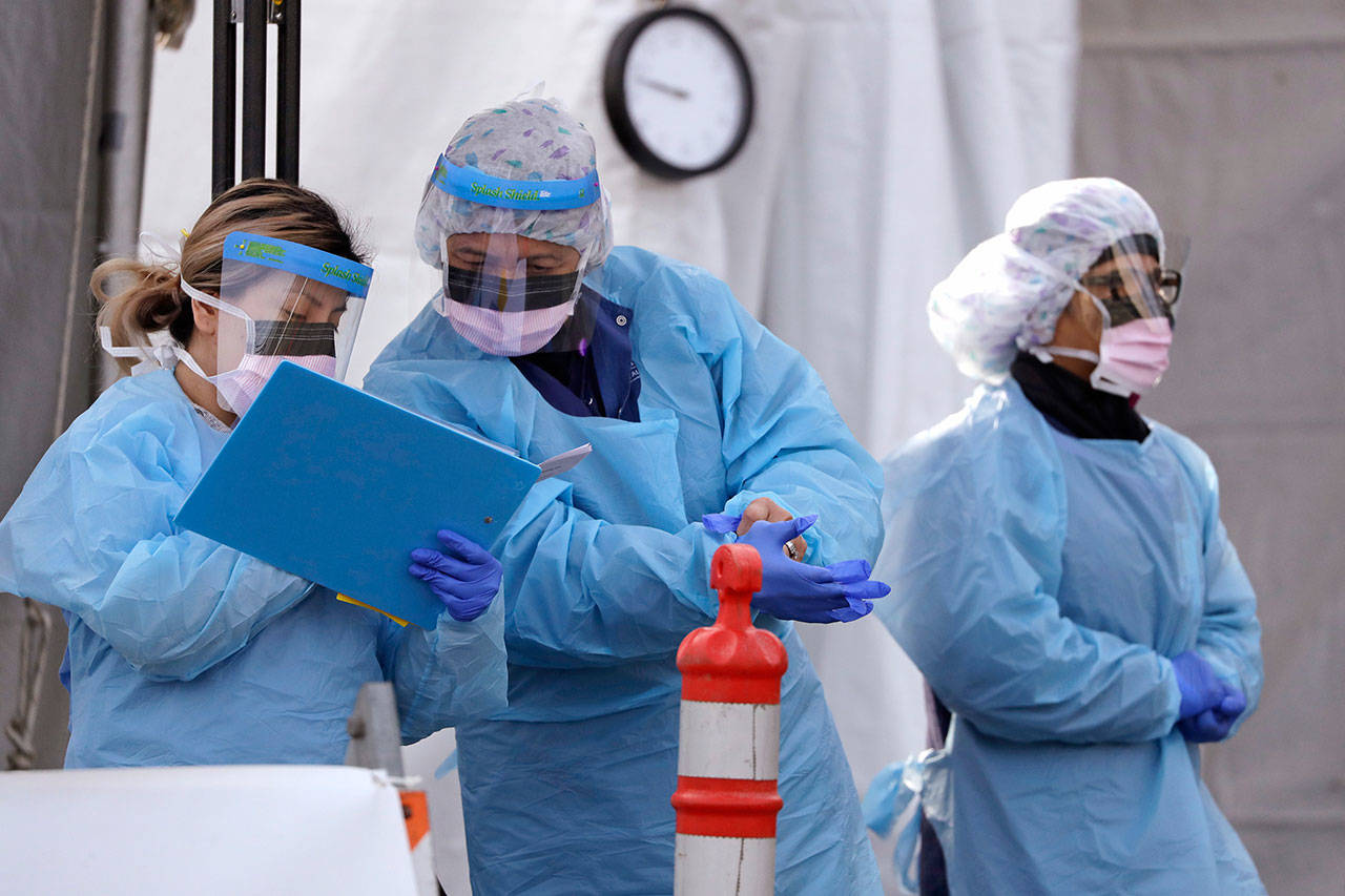 Medical personnel complete administrative work after testing a patient up at a drive-through coronavirus testing station for University of Washington Medicine patients March 17, in Seattle. Health authorities in Washington reported more Covid-19 deaths in the state that has been hardest hit by the outbreak. (Elaine Thompson / Assocaited Press)