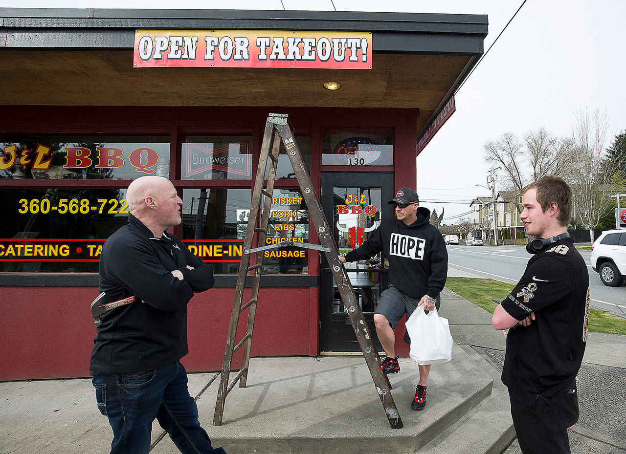 J & L BBQ owner Joel Sexton (left) talks with customer Tony Cecsarini and Austin Eisenhuth (right) after hanging banners announcing the restaurant’s ability to accept takeout orders on Tuesday in Snohomish. (Andy Bronson / The Herald)