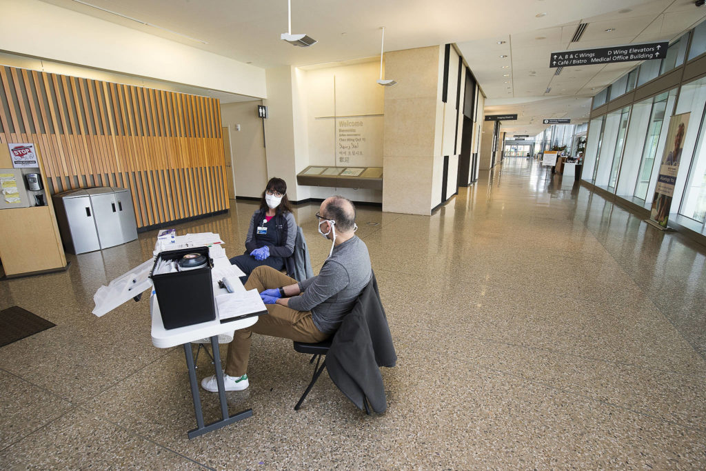 In a normally bustling hospital lobby, Amanda Ray and Deniz Campbell man a security screening desk at Providence Regional Medical Center on Friday, March 20, 2020 in Everett, Wa.(Andy Bronson / The Herald)
