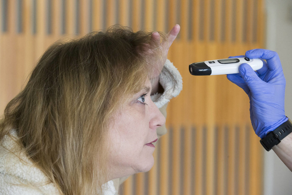 Susan Kaylor pulls her hair back to have her forehead temperature taken at Providence Regional Medical Center on Friday, March 20, 2020 in Everett, Wa.(Andy Bronson / The Herald)
