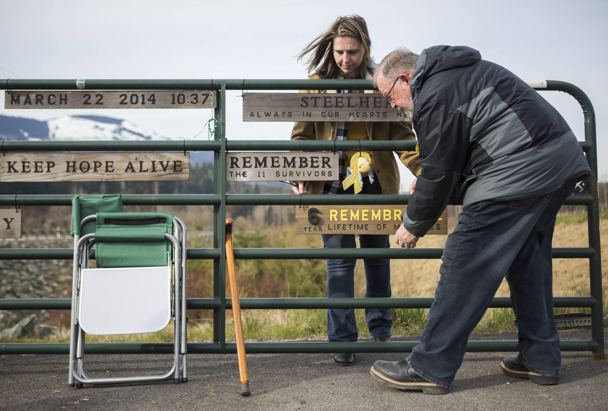 Jennifer Thompson, left, and her father Ron Thompson secure a new remembrance plaque to the Oso slide site gate on Sunday, near Oso. Ron Thompson handcrafts a new plaque for the gate every year. (Olivia Vanni / The Herald)