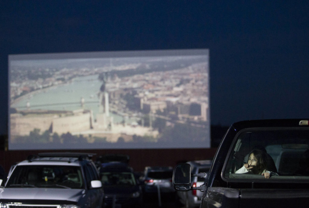 A young girl plays in in the back seat of a pick-up truck as movie previews play on the drive-in screen on Thursday. (Olivia Vanni / The Herald)
