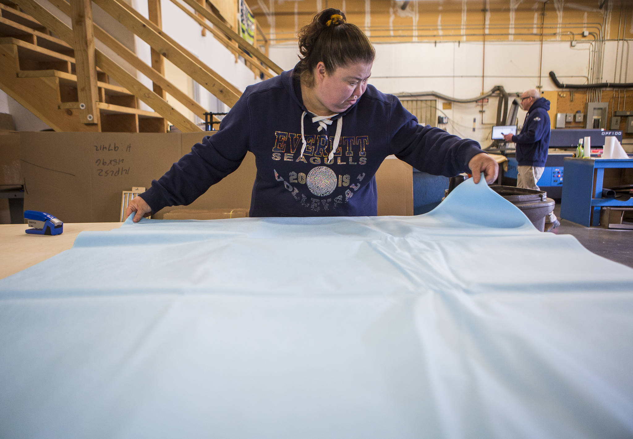 Tami Carrero lines up surgical wrap for face masks to be cut into straps and mask pieces Friday at Terrene Inc. in Mukilteo. The fabrication company specializes in laser work but modified operations to produce face masks for healthcare workers. (Olivia Vanni / The Herald)