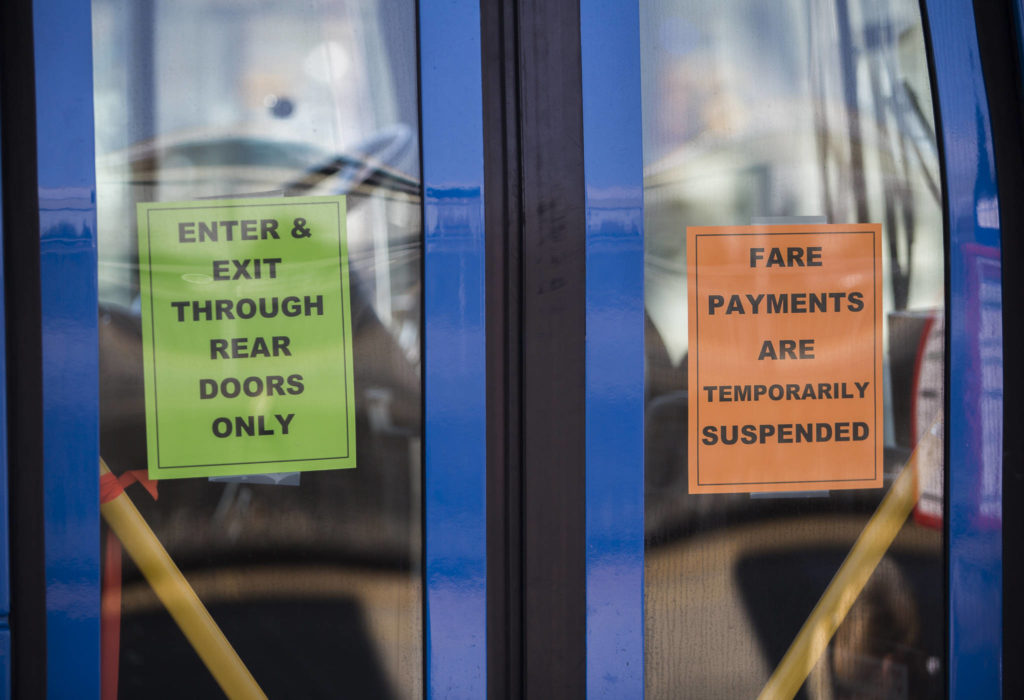 Two signs on the front door of a Community Transit bus direct riders to the rear doors and alert them that payments are suspended. (Olivia Vanni / Herald file)
