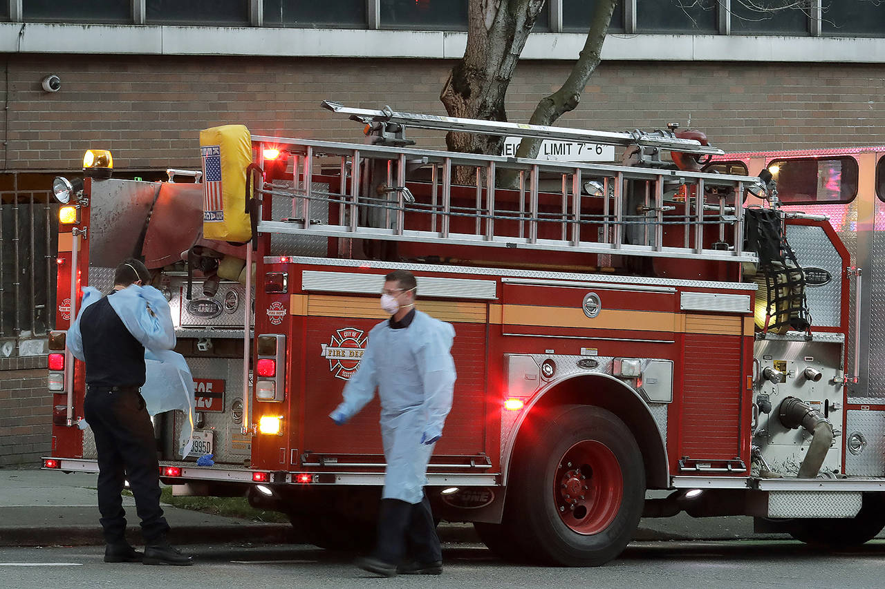 Seattle firefighters wearing masks, gowns, and gloves to protect against the transmission of the new coronavirus, walk and stand near their engine after responding to a medical call in Seattle on Tuesday. (AP Photo/Ted S. Warren)