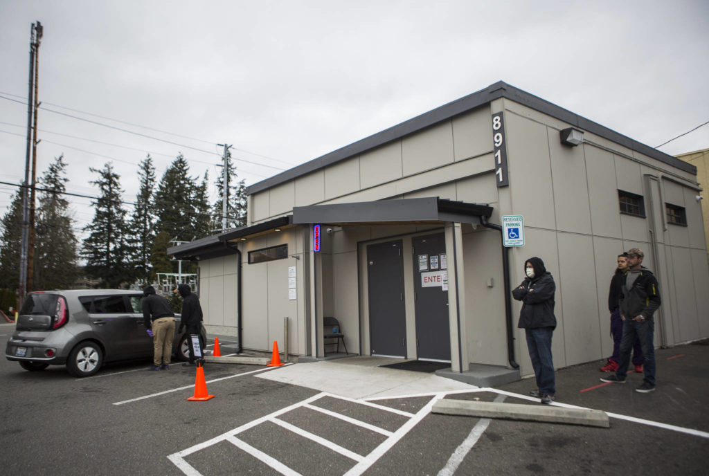 Kushman’s employees run a curbside pickup order to a customer while others wait in line, six feet apart, outside of the building on Friday in Everett. (Olivia Vanni / The Herald) 
