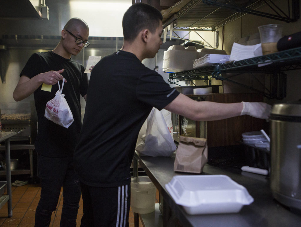 Anthony Luong (left) checks an order ticket while Brian Le works on packaging up food at Basil Authentic Vietnamese Cuisine on April 5 in Everett. (Olivia Vanni / The Herald)
