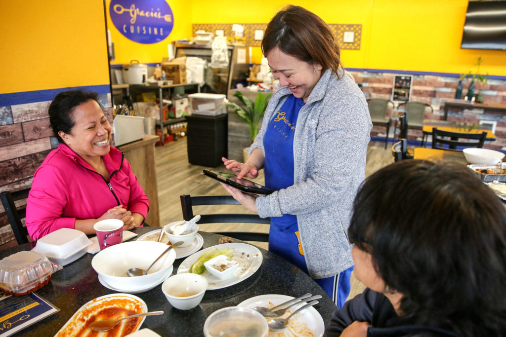 Grace Correa (center) owner-operator, totals a check for Merlyn Gustafson (left) and Jojie Villaroya at Gracie’s Cuisine Saturday afternoon in Everett on March 14. Two days later, sit-down dining was banned in restaurants across the state. (Kevin Clark / The Herald)
