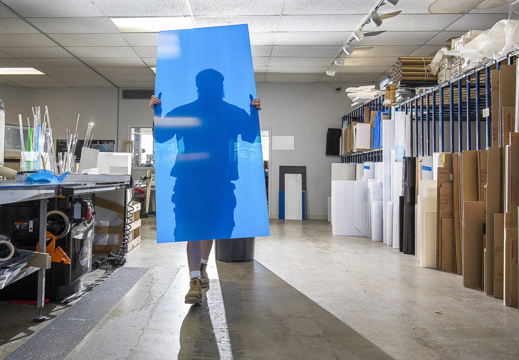 Store Manager Ben Winslow cuts sheets of plastic for customers’ orders at Tap Plastics on April 6 in Everett. The cut sheets will be made into sneeze guards and face masks. (Andy Bronson / The Herald)
