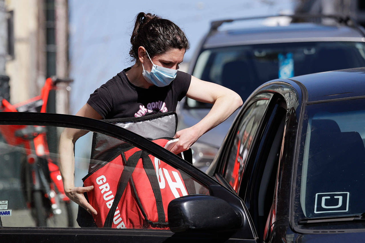 Food delivery driver Dori McGuire Guy wears a protective mask as she loads a take-out order into her car at the Pike Place Market, March 20, in Seattle. (Elaine Thompson / Associated Press)