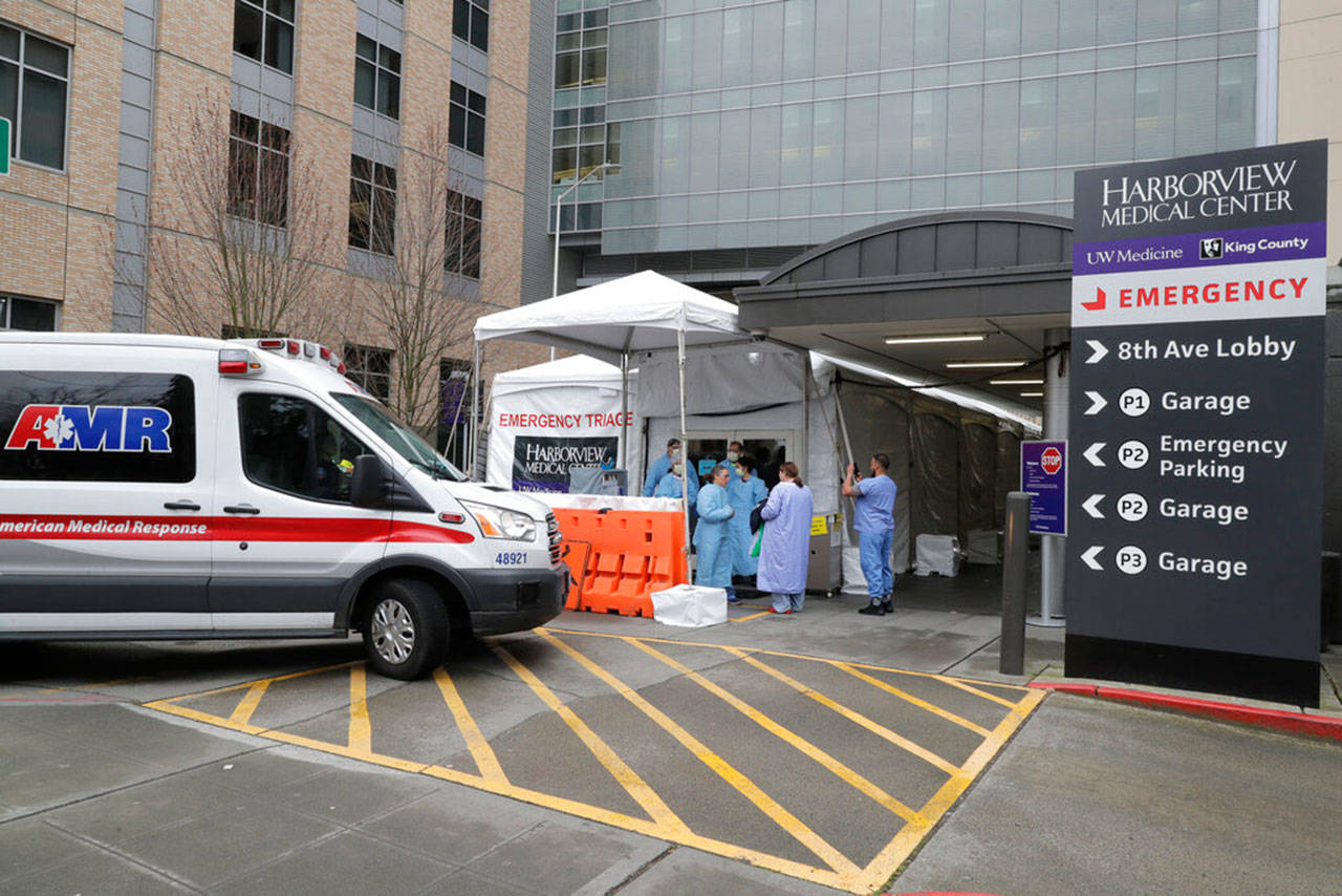 An ambulance pulls up as nurses outside a triage tent for the Emergency Department at the Harborview Medical Center in Seattle put on gowns and other protective gear at the start of their shift, April 2. The tent, which was recently put in place, is used to examine walk-up and other patients who arrive at the emergency room with respiratory symptoms possibly related to the COVID-19 coronavirus. (Ted S. Warren / Associated Press)