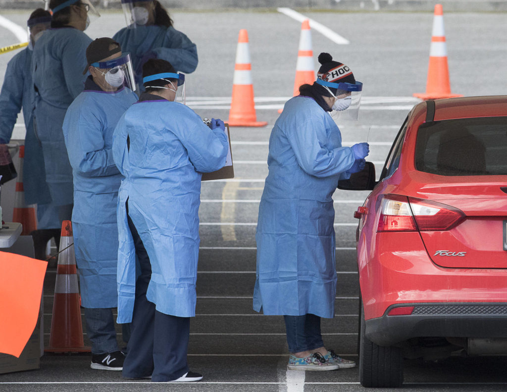 Medical workers test for the COVID-19 virus at a drive-thru testing site in the parking lot near Everett Memorial Stadium at 3900 Broadway on Monday in Everett. Only patients with referrals from a doctor are tested, after setting up an appointment. (Andy Bronson / The Herald)
