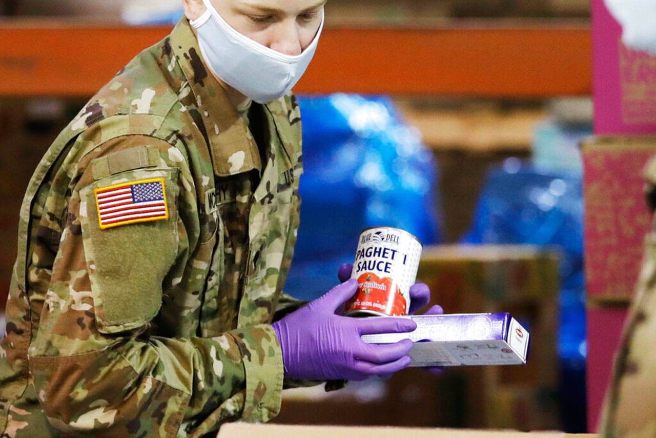 A Washington National Guardsman packs food at the Nourish Pierce County warehouse in response to the coronavirus outbreak Friday, in Lakewood. National Guard members will be packing food at the warehouse five days a week for delivery to multiple food banks, taking over for volunteers who normally pack several hundred boxes a day. The need for food at the pantries in the area is expected to at least double in the coming weeks as a state stay-at-home mandate has been extended until at least May 5. (Elaine Thompson / Associated Press)