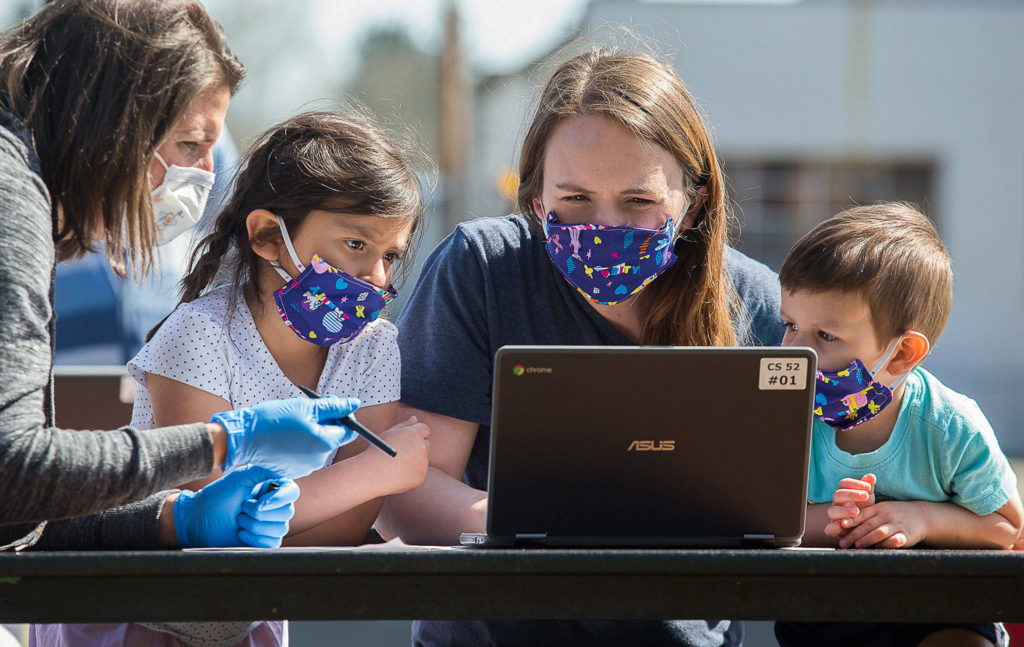 Jody Urban, left, helps Michelle Nunez setup a Chromebook at Frank Wagoner Elementary School as her daughter Lilah, left, and son Oilver watch. Students and their families picked up computers for online learning on Wednesday. (Andy Bronson / The Herald)
