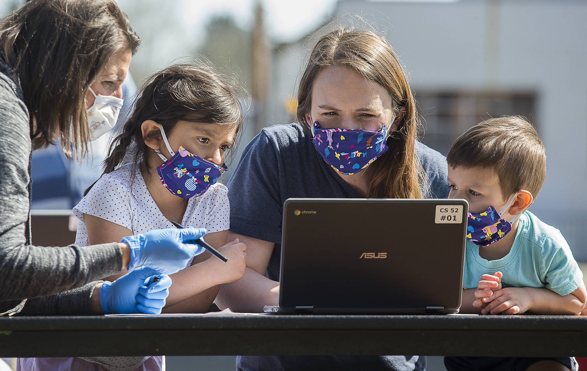 Jody Urban, left, helps Michelle Nunez setup a Chromebook at Frank Wagoner Elementary School as her daughter Lilah, left, and son Oilver watch. Students and their families picked up computers for online learning on Wednesday. (Andy Bronson / The Herald)