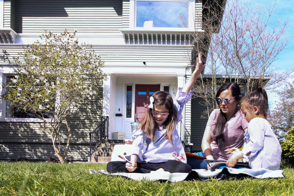 Paige Bone, 7, (left to right), celebrates finishing her timed math assignment with mother Aisha Bone and sister Poppy Bone looking on Friday morning at their home in Everett on April 17, 2020. (Kevin Clark / The Herald)
