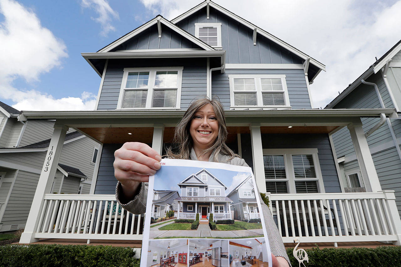 In this April 1 photo, Rebeka McBride holds a picture of her home as she poses in front of it in Monroe, Washington. She put her house on the market in early March and is in the process of closing on the sale. (AP Photo/Elaine Thompson)