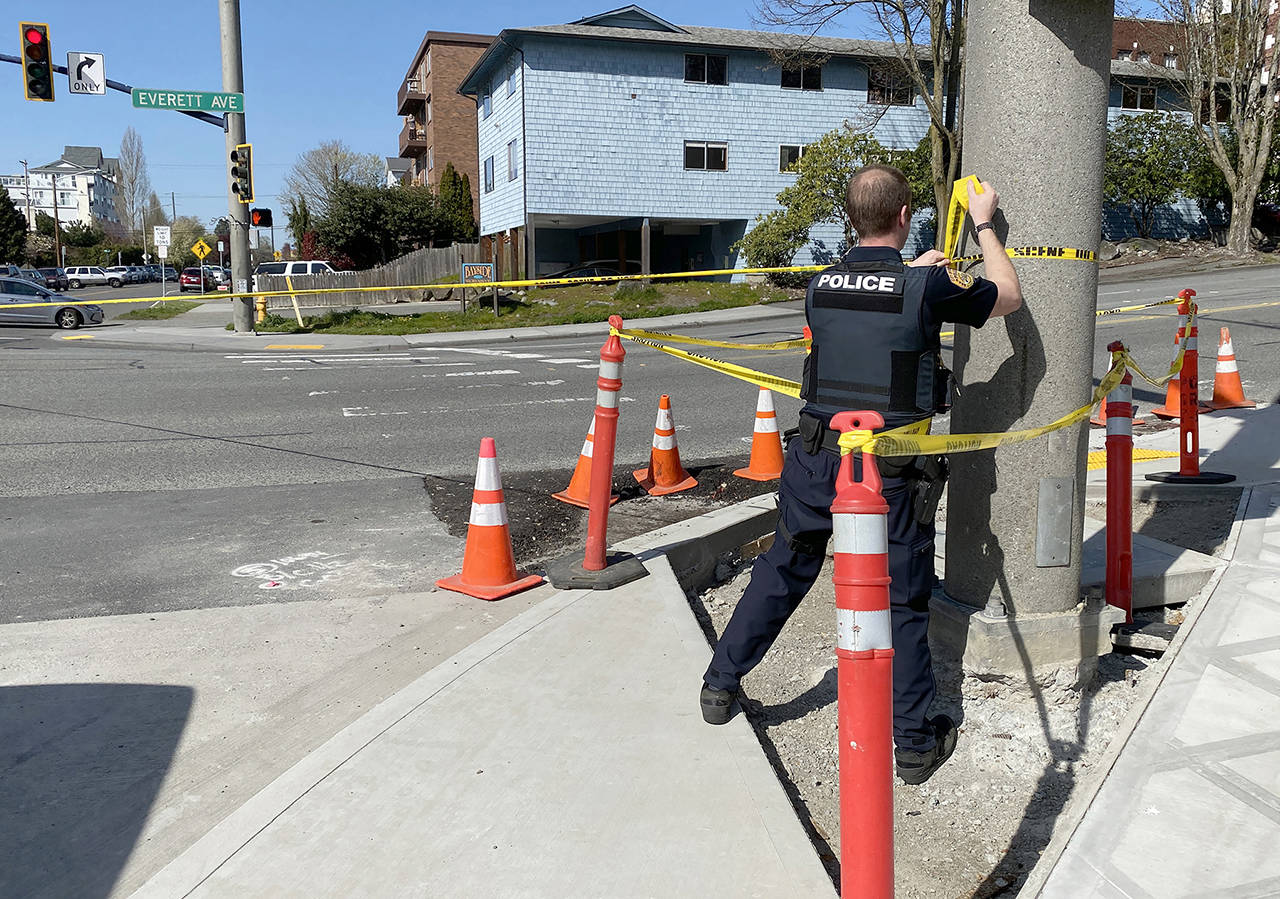 A police officer attaches yellow tape to a traffic light pole at the scene of a fatal shooting Thursday afternoon in northwest Everett. (Sue Misao / The Herald)