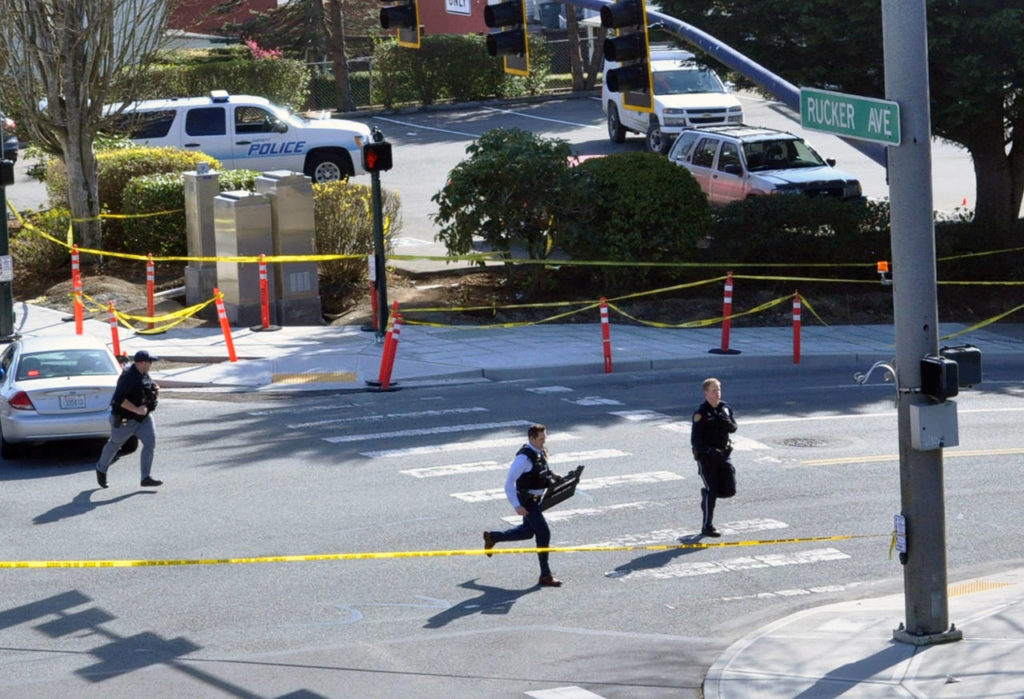 During the investigation of a shooting Thursday in northwest Everett, police run toward an apartment building across Everett Avenue near the taped-off crime scene. (Sue Misao / The Herald)
