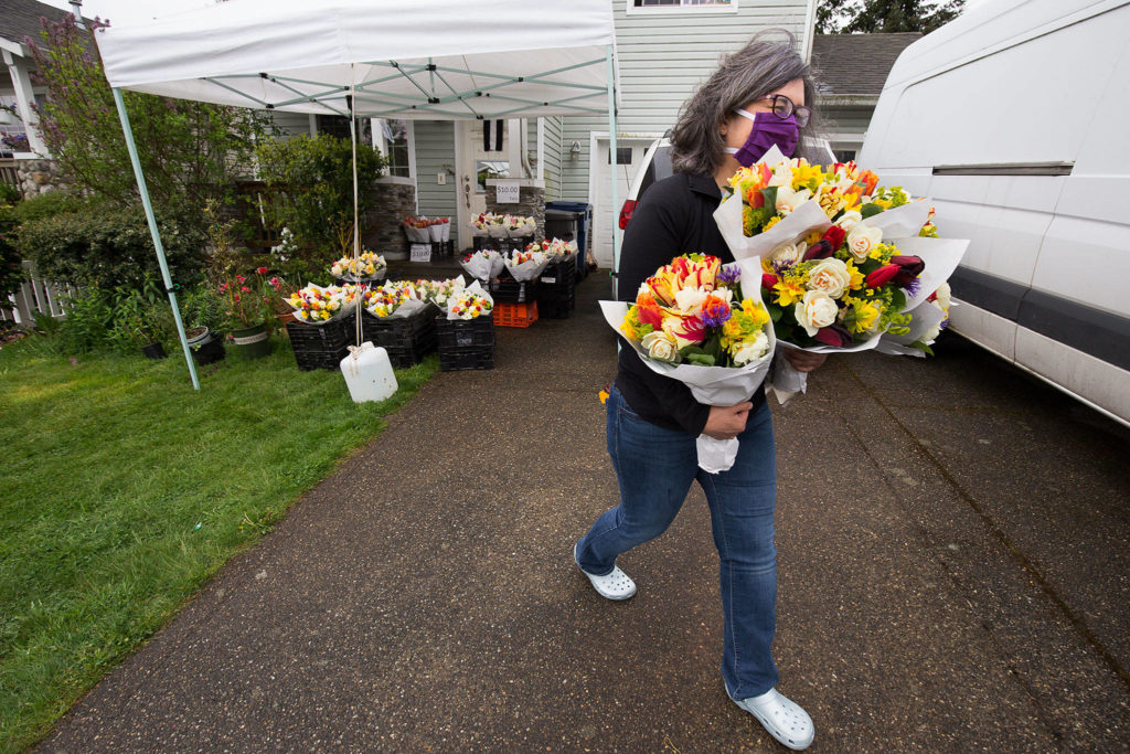 Gina Corpening carries off an armful of bouquets from Teng’s Garden sold from the flower farm family’s front porch in Everett. Teng’s Garden and other flower vendors initially were prohibited from farmers markets because of public health restrictions, but now can sell after the state weighed in. (Andy Bronson / The Herald)
