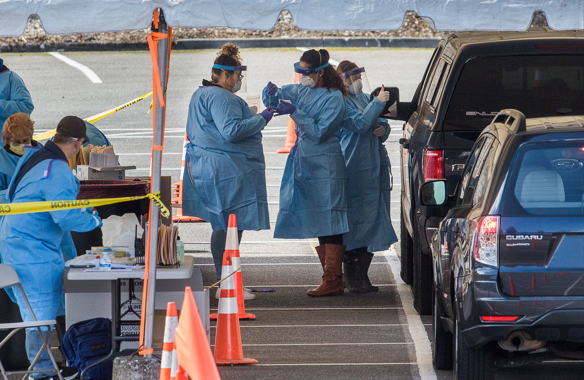 One medical worker gives a thumbs up as two others collect a swab after a test for the COVID-19 virus at a drive-thru testing site in the parking lot near Everett Memorial Stadium at 3900 Broadway on March 23 in Everett. (Andy Bronson / Herald file)