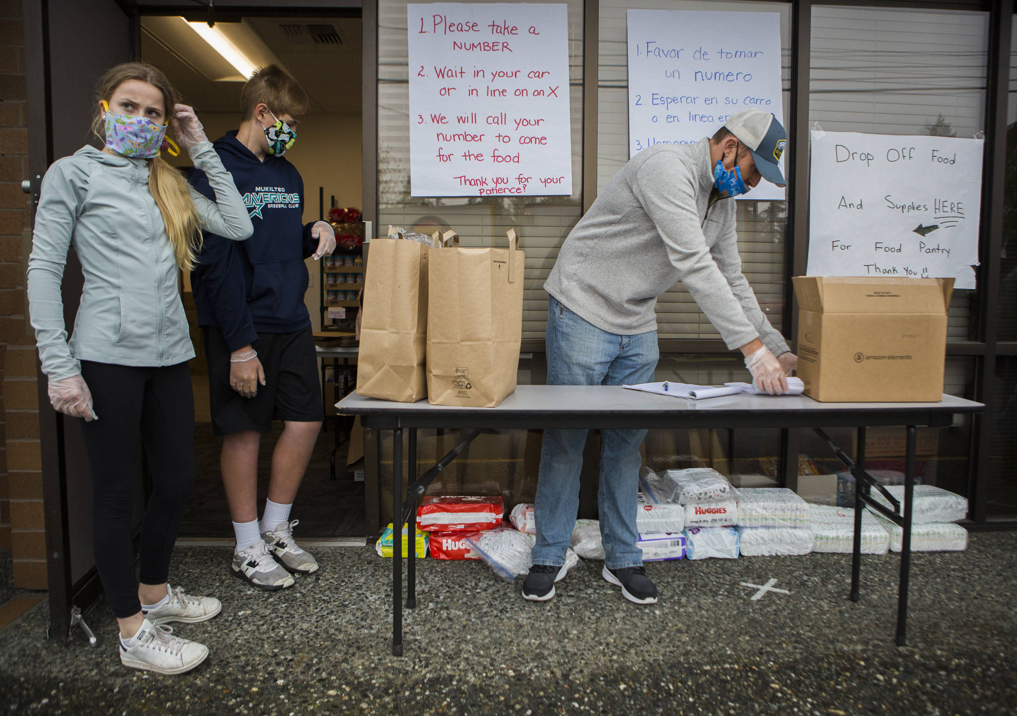 Reese Jordan (left) and Cole Armstrong-Hoss (center) wait for instructions from Cory Armstrong-Hoss (right) as they set up to open the temporary food bank at The Village on April 21 in Everett. (Olivia Vanni / The Herald)