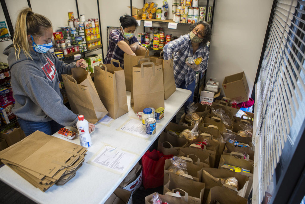 Taylor Eines (left), Akari Takayama (center) and Marilyn Robles (right) put together food bags for people to pick up at The Village on April 21 in Everett. (Olivia Vanni / The Herald)
