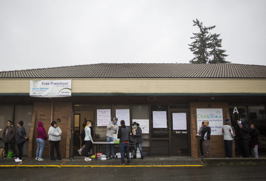 People line up and wait for their numbers to be called to pick up food April 21 outside of The Village in Everett. (Olivia Vanni / The Herald)
