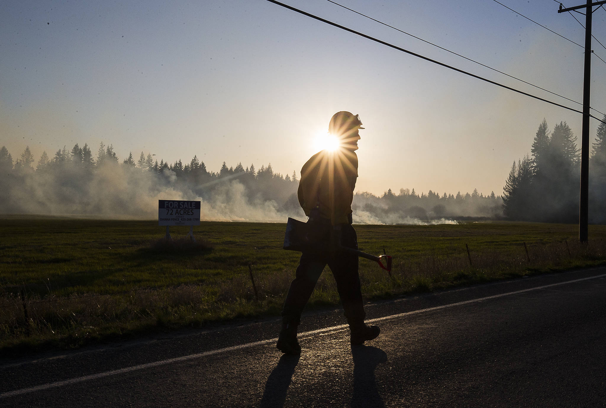 Snohomish County Fire District 21 firefighter Trent Nunemaker walks along Highway 9 as he and others fight a large brush fire Wednesday in Bryant. (Andy Bronson / The Herald)