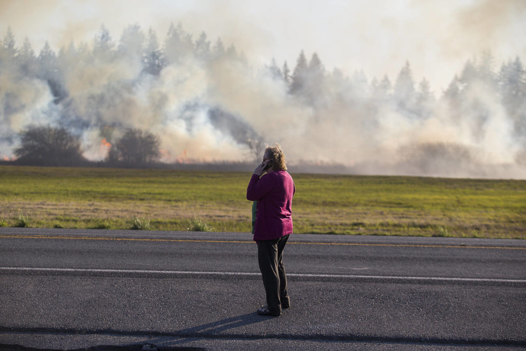 A woman watches as fire spreads across her property while multiple strike teams from Snohomish County fire departments fight a brush fire along Highway 9 on Wednesday in Bryant. (Andy Bronson / The Herald)
