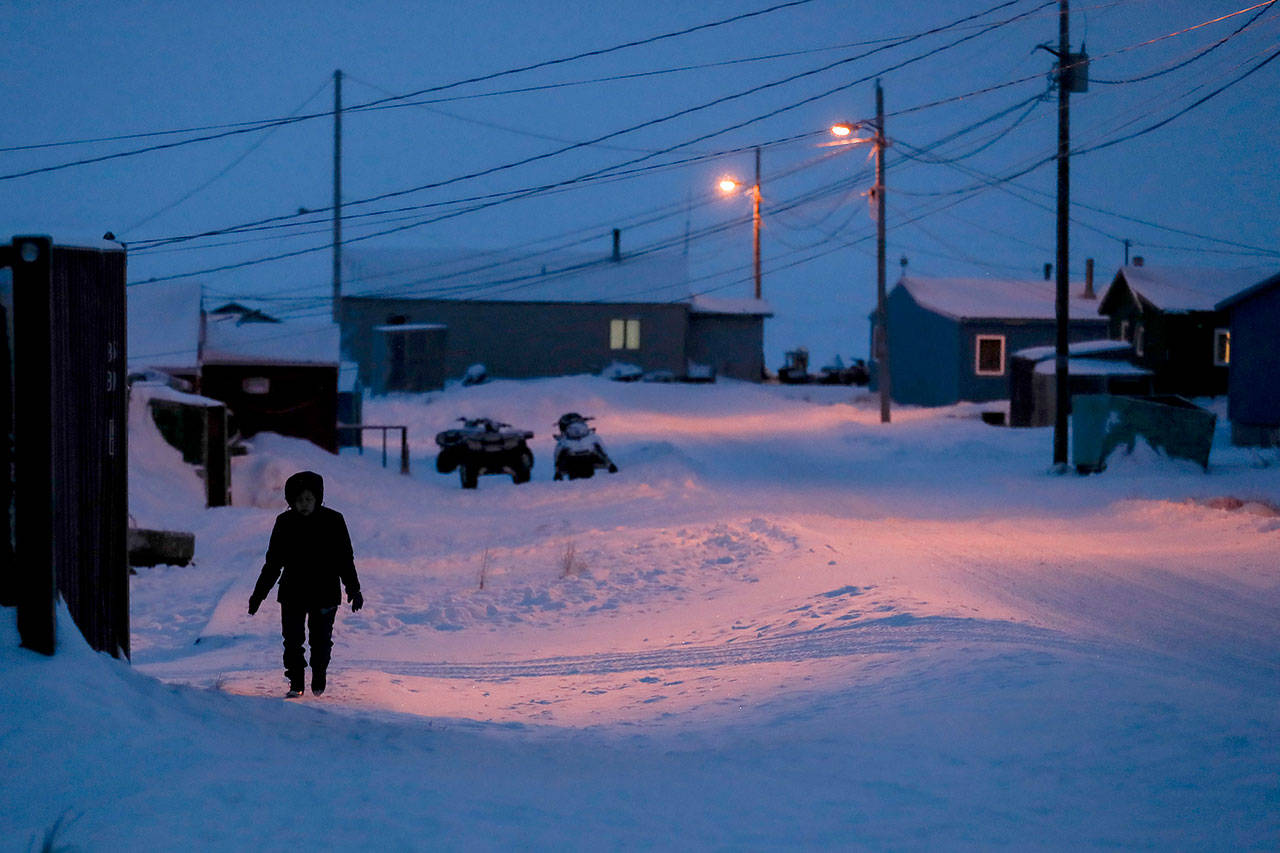 In this Jan. 20 photo, a woman walks before dawn in Toksook Bay, Alaska, a mostly Yuip’ik village on the edge of the Bering Sea. Native American leaders are raising questions about how $8 billion in federal coronavirus relief tagged for tribes will be distributed, with some arguing that for-profit Alaska Native corporations shouldn’t get a share of the funding. (AP Photo/Gregory Bull, File)