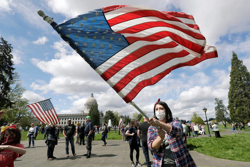 Janell Sorensen, of Woodland, waves a flag Sunday as demonstrators begin to gather at the Capitol in Olympia for a protest opposing Washington state’s stay-home order to slow the coronavirus outbreak. (AP Photo/Elaine Thompson)
