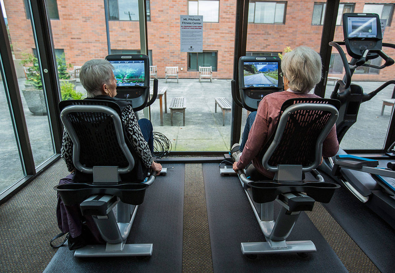 Jean Kinity (left) and Sandra Barton chat as they try out recumbent bikes at the Carl Gipson Senior Center’s fitness room in October 2019 in Everett. The senior center was closed following the coronavirus outbreak and may remain closed through 2021 because of pending city budget cuts. (Olivia Vanni / The Herald)