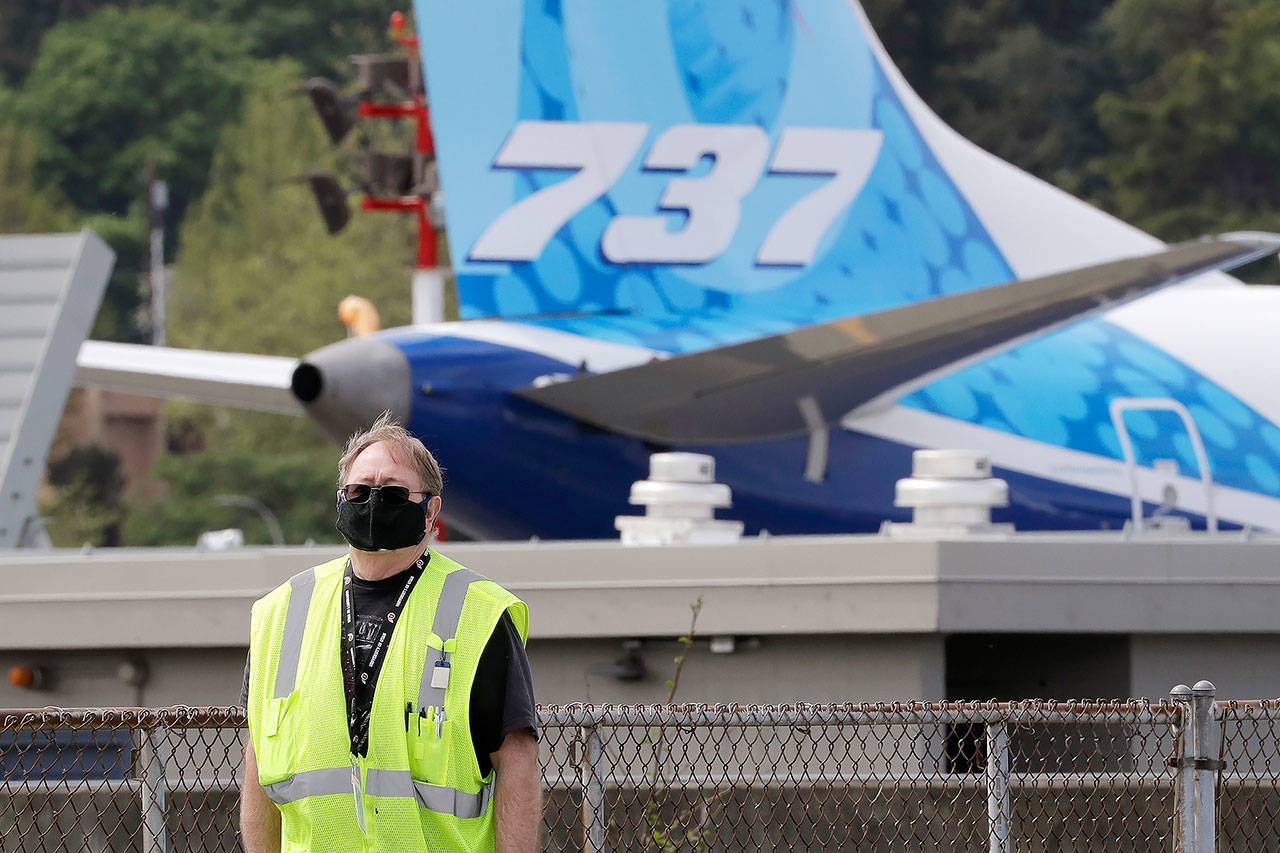 A masked worker walks in view of a 737 jet at a Boeing airplane manufacturing plant Wednesday in Renton. (AP Photo/Elaine Thompson)