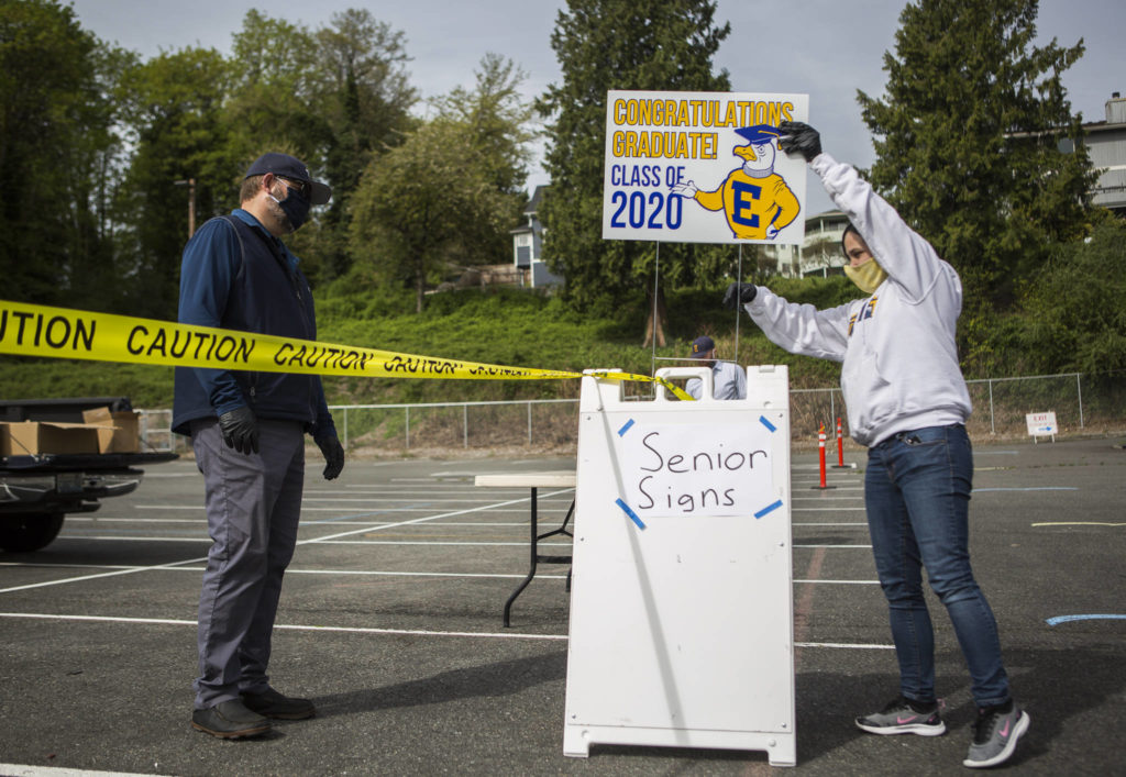 Doug Plucker (left) and Mary Ingraham (right) set up signs for seniors to pick up at the drive-thru graduation gown pickup Tuesday in Everett. (Olivia Vanni / The Herald)

