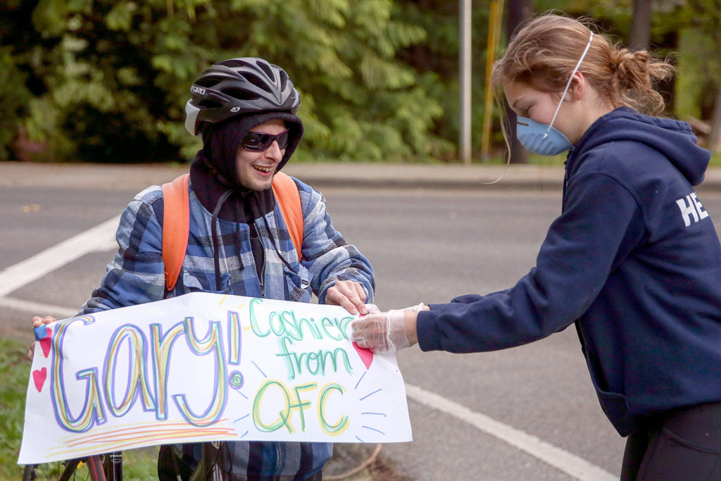Annabelle Heiman (right) attaches a sign to Gary Locke’s bike in preparation as guest of honor in a parade down 53rd Avenue West in Mukilteo. The block does a “2 minutes of gratitude” nightly tribute to those on the frontlines. (Kevin Clark / The Herald)

