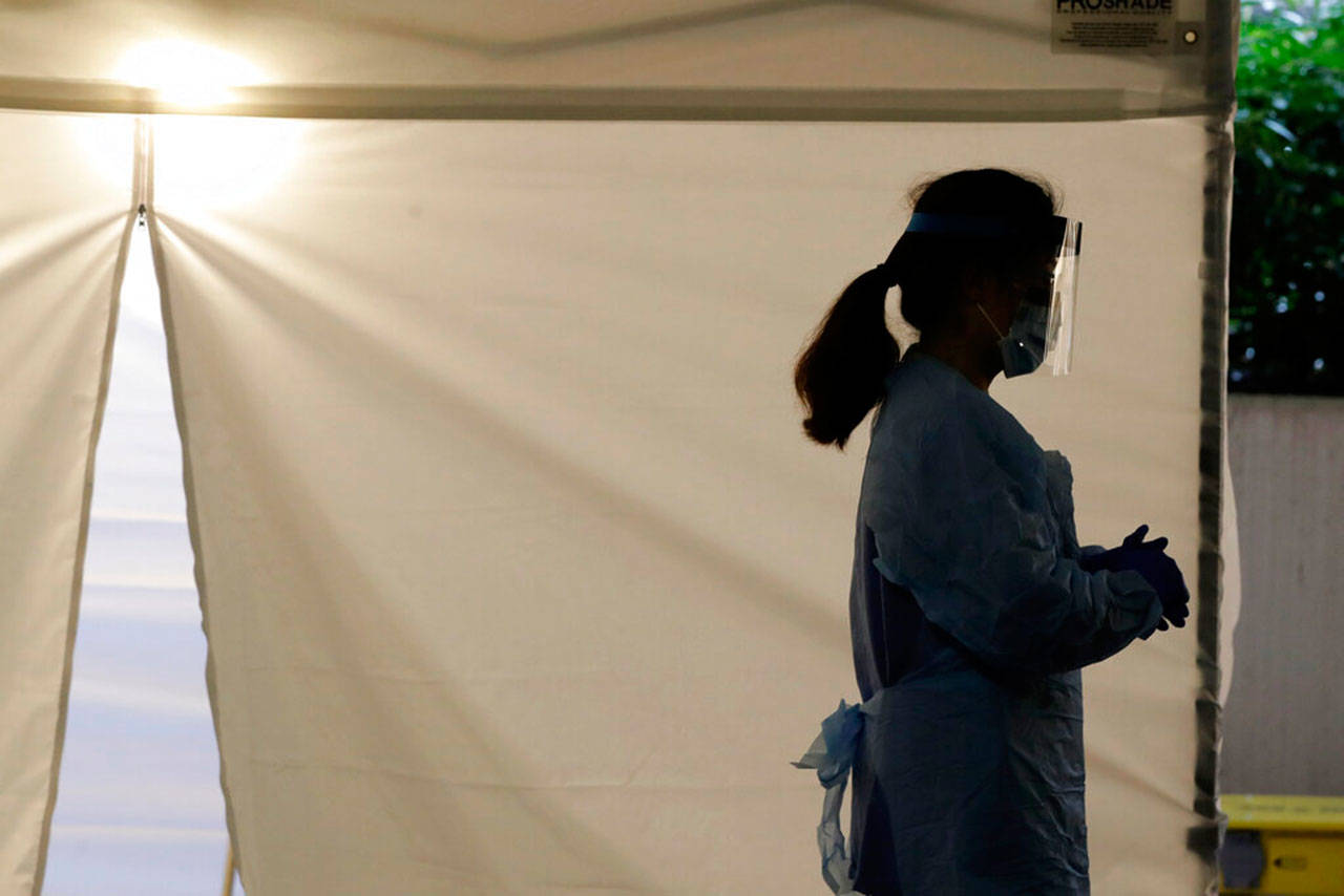 A nurse at a drive-up coronavirus testing station set up by the University of Washington Medical Center waits by a tent in Seattle in March. Between now and 2025, there will be a shortage of some 7,000 registered nurses in Washington state, according to a federal nursing worforce survey (Ted S. Warren / Associated Press file photo)