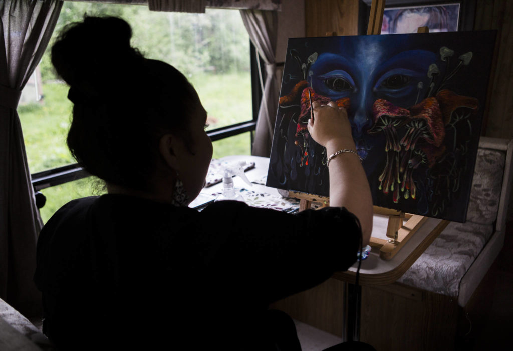 A woman works on her paintings with black light reactive acrylic paint at her home on Sunday in Everett. She is a self-taught painter who has been living and painting in Snohomish County for more than 18 years. (Olivia Vanni / The Herald)

