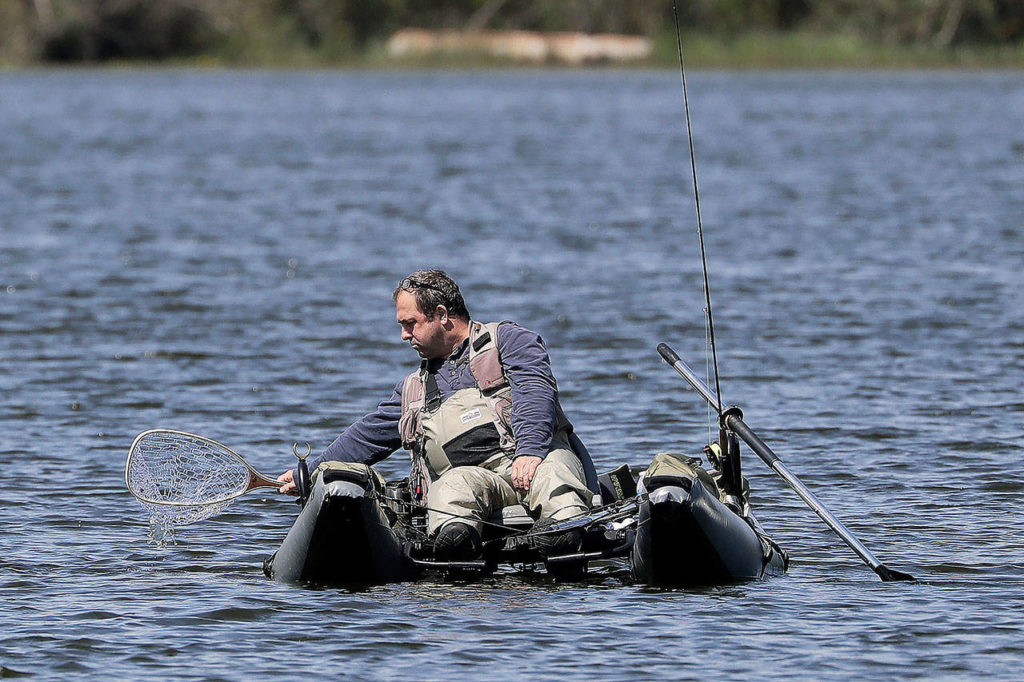 An angler dips his net into Blackmans Lake while fishing on the first day of a partial reopening of outdoor recreation activities Tuesday. in Snohomish. Hunting, fishing and golf are allowed under Phase 1 of the state’s plan for reopening. (Elaine Thompson / Associated Press)
