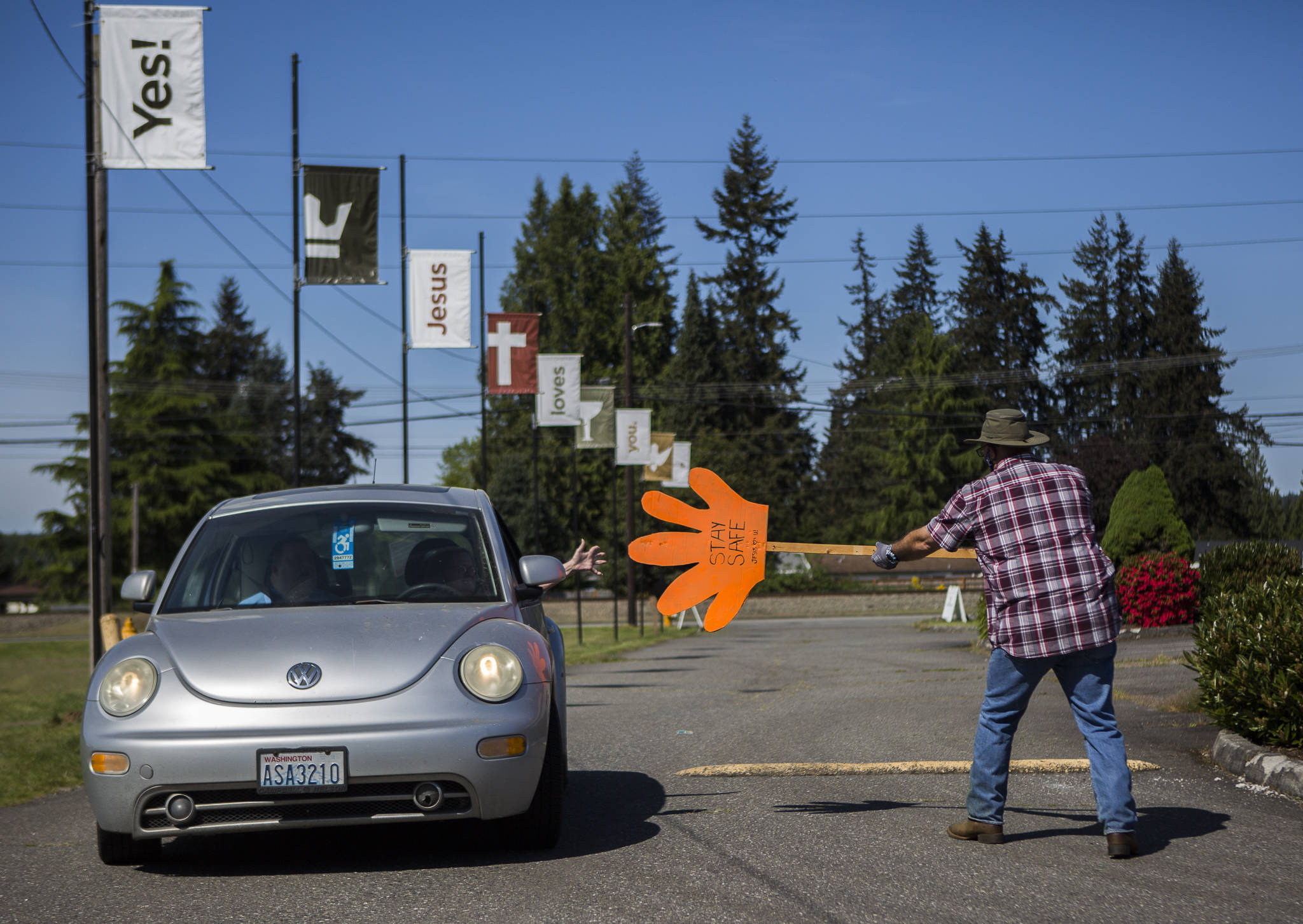 Arthur Bender (right) high-fives drive-in churchgoers as they arrive for parking lot services at Marysville Foursquare Gospel Church on Sunday. (Olivia Vanni / The Herald)