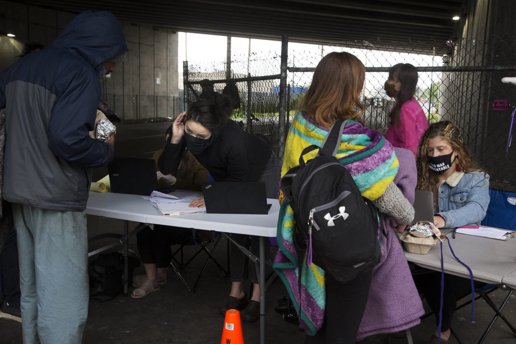 With I-5 traffic overhead making it difficult to hear, Sarah Alvarez cups her ear to listen to a man talk as volunteers with Angel Resource Connection help homeless people sign up for stimulus checks in Everett. (Andy Bronson / The Herald)
