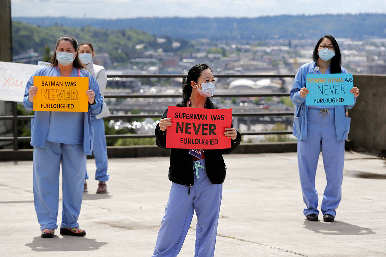 Health care workers Mechelle Cannon (left), Chiow Saechao (center) and Gina Tualla stand in protest with other staff at Harborview Medical Center, a part of UW Medicine, during a noon hour break in a demonstration asking management to do more to protect staff, patients and the public amid the COVID-19 pandemic, Thursday in Seattle. (AP Photo/Elaine Thompson)
