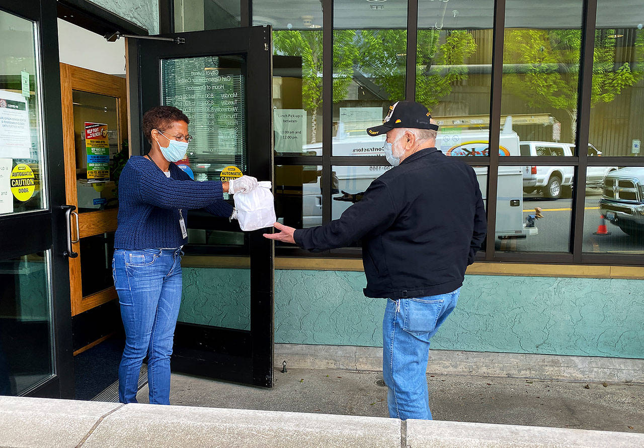Elizabeth What-Hall, at Carl Gipson Senior Center in Everett, hands a sack lunch to Duane Conklin on Tuesday morning. (Sue Misao / The Herald)