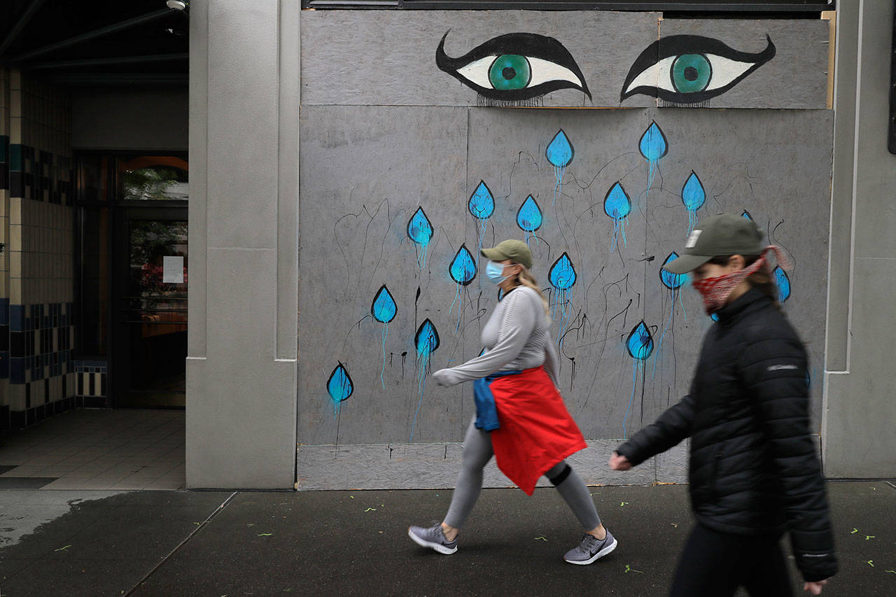 Pedestrians wearing face masks walk past art by Patricia Rovzar on her boarded-up art gallery, May 16, in downtown Seattle. On Saturday, officials reported that Washington state had reached the grim milestone of 1,000 deaths from the coronavirus. (Ted S. Warren / Associated Press)