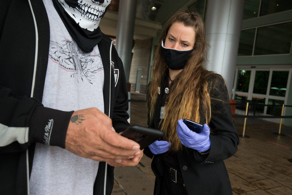 Victoria Blymyer checks in a customer as the Tulalip Resort Casino reopens Tuesday. To control attendance, a customer must submit a request, then wait for a text that notifies them when they may enter — after screening. (Andy Bronson / The Herald)
