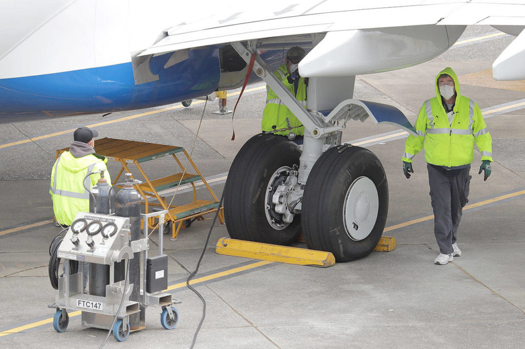 Boeing Co. employees wearing masks work near the landing gear of a 737 Max last month in Renton. (AP Photo/Ted S. Warren) 
