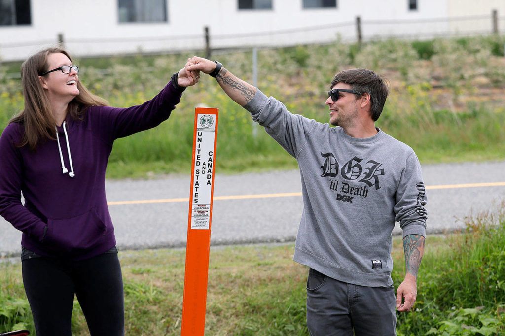 In this May 17 photo, Kris Browning (left) stands in Canada and holds hands with her husband, Tim Browning, in the U.S., after posing for a photo at the border near Lynden, Washington. With the border closed to nonessential travel amid the global pandemic, families and couples across the continent have found themselves cut off from loved ones on the other side. (AP Photo/Elaine Thompson)
