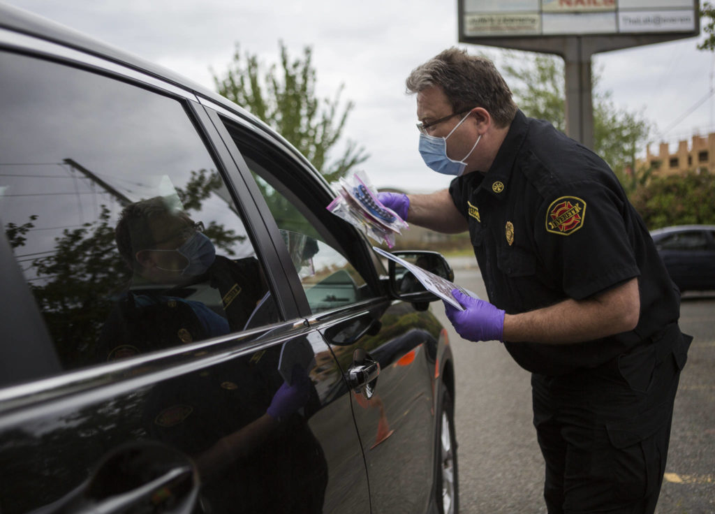 Brent Stainer, director of Everett Emergency Management, hands out masks at a free face-mask drive-thru recently in the WSU Everett parking lot. (Olivia Vanni / The Herald)
