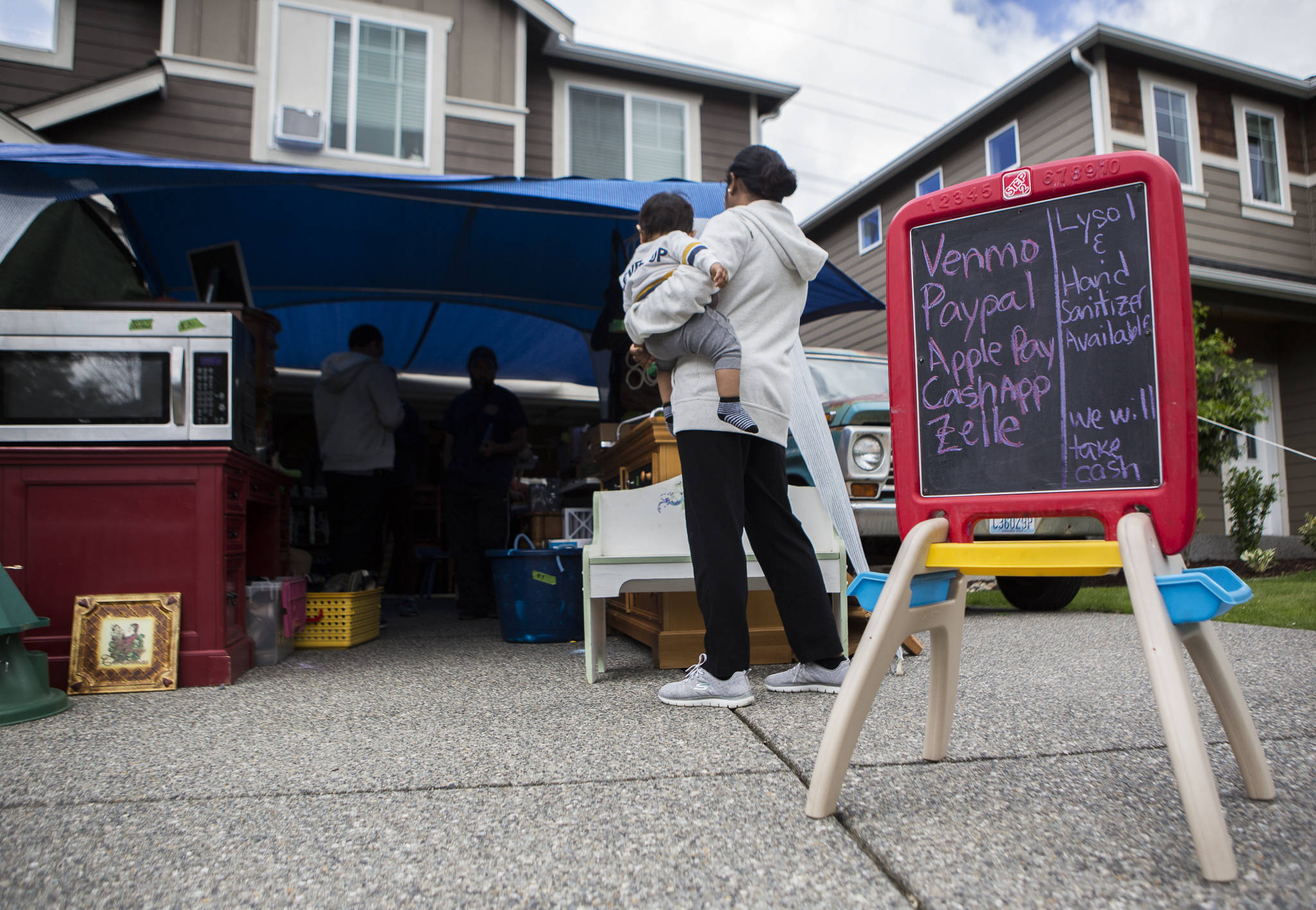 A sign offering different payment methods and disinfecting options for customers stands next to the entrance of the Carter family’s garage sale on Sunday in Bothell. Yard sales and garage sales were one of the things allowed again in Gov. Jay Inslee’s Phase 2 reopening plan. (Olivia Vanni / The Herald)