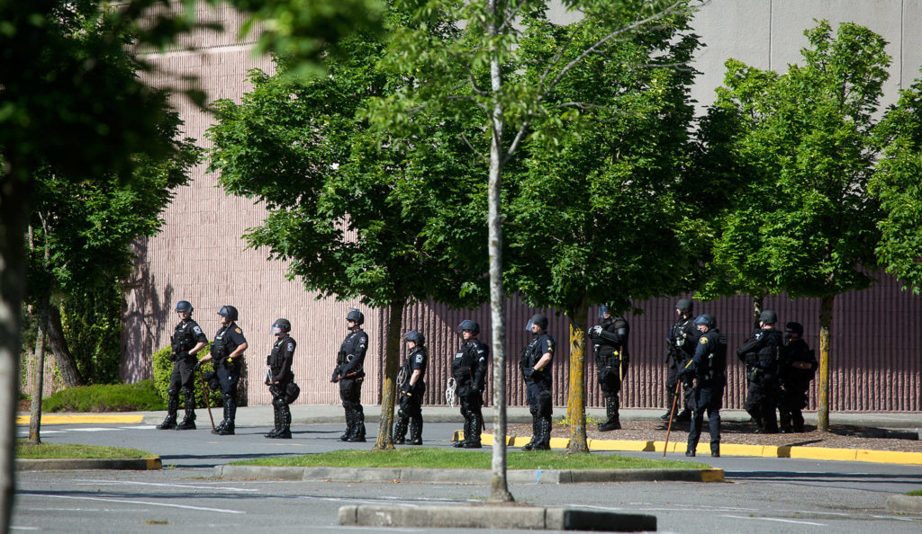 Watching a group of people walking the sidewalk, after they walked past barricaded streets, law enforcement officers from a line in front of the Alderwood mall on Monday in Lynnwood. (Andy Bronson / The Herald)
